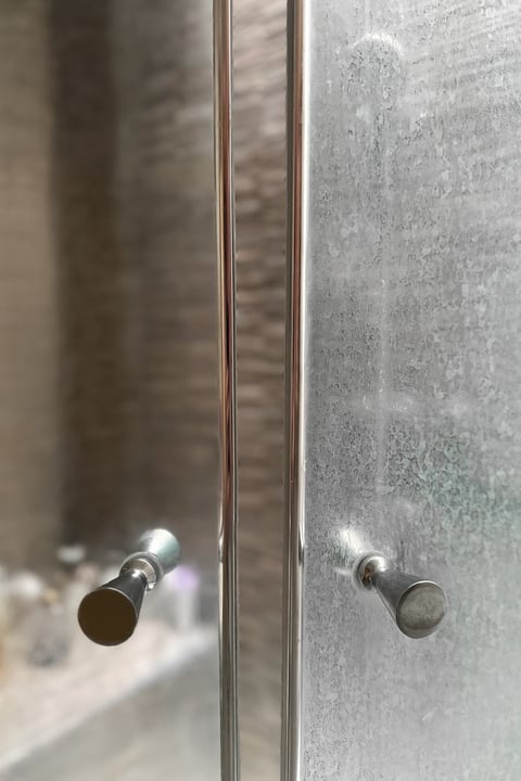 Close-up of a dirty shower glass door with white mineral residue from hard water and soap scum.Another side of the door after cleaning. Blurred shower cabin in the background. Common bathroom cleaning issue.